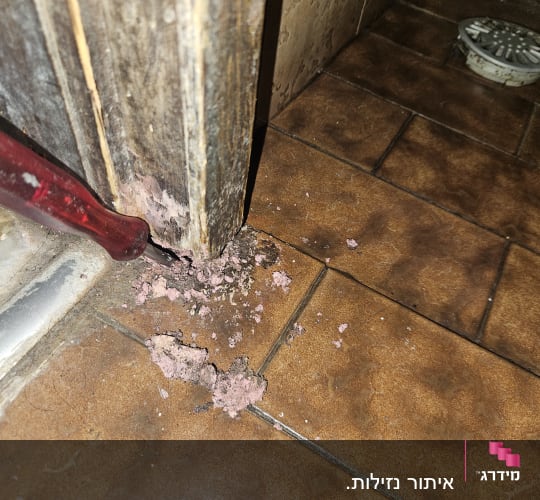 מברג ליד דלת עם סימני ריקבון על הרצפה